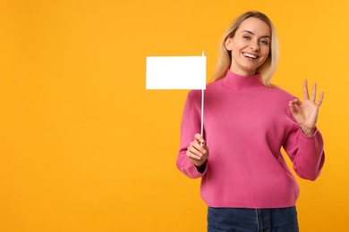 Happy woman with blank white flag showing OK gesture on orange background. Mockup for design