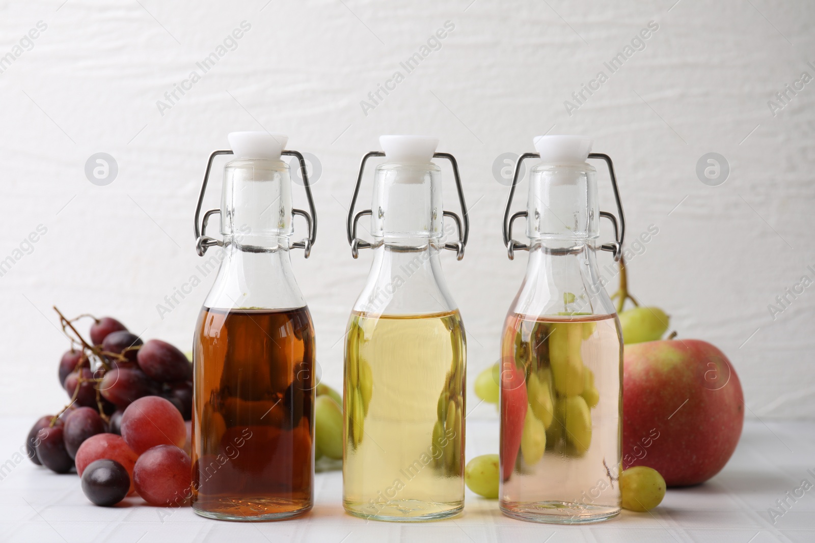 Photo of Different types of vinegar and ingredients on light tiled table, closeup