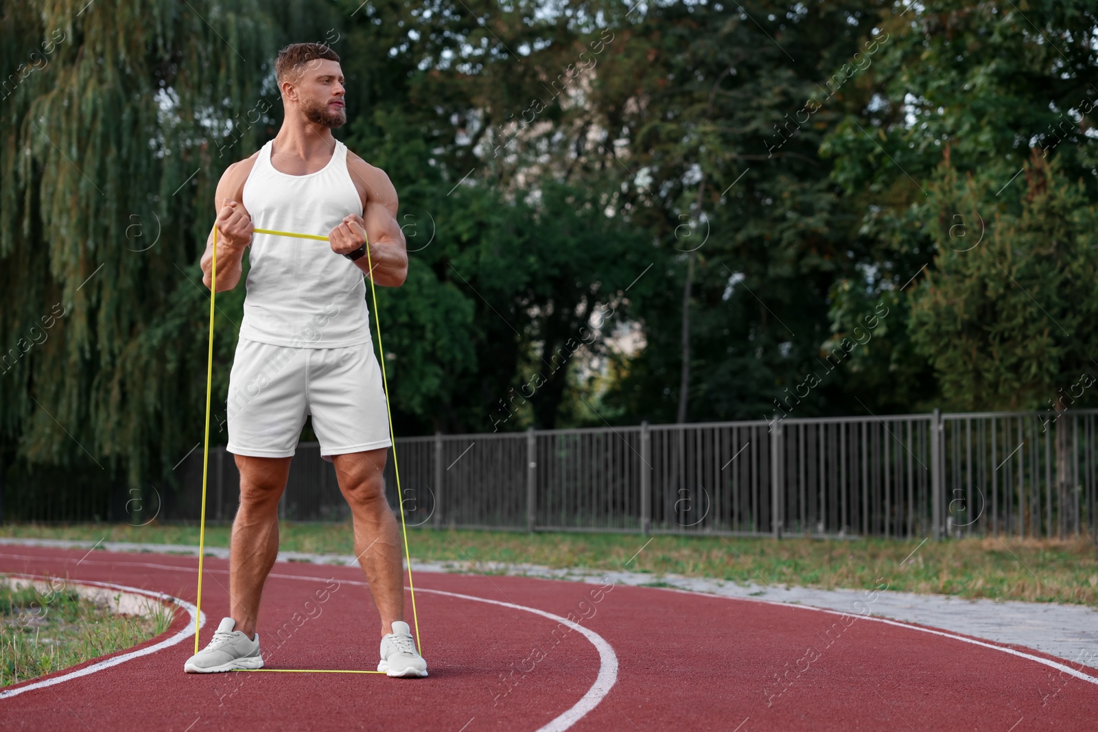 Photo of Muscular man doing exercise with elastic resistance band at stadium