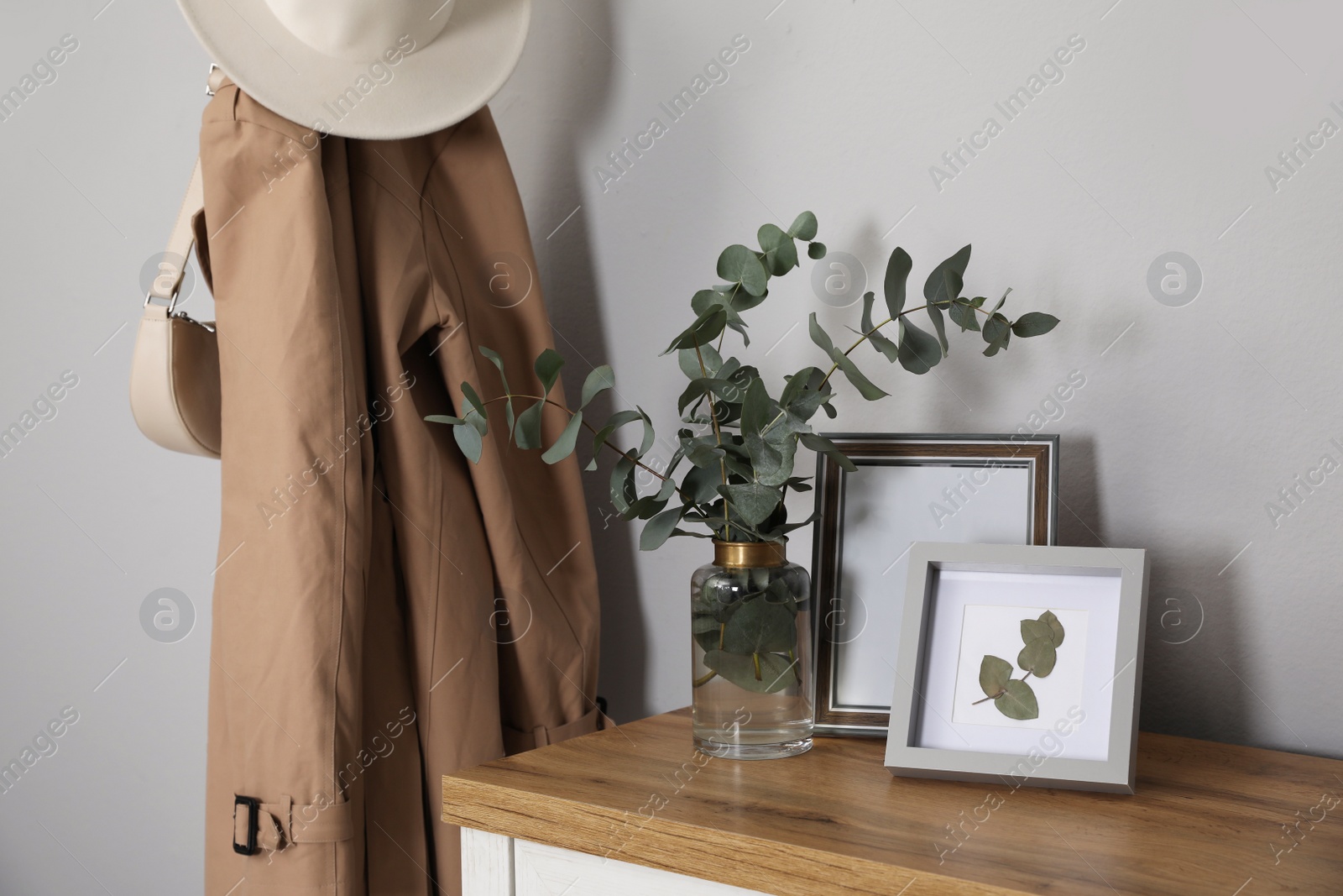 Photo of Vase with beautiful eucalyptus branches and pictures on chest of drawers near grey wall