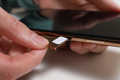 Photo of Woman putting SIM card tray in smartphone at white table, closeup