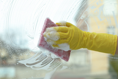 Woman cleaning window with sponge at home, closeup