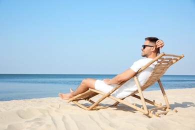 Photo of Young man relaxing in deck chair on sandy beach