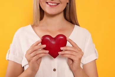 Happy volunteer holding red heart with hands on orange background, closeup