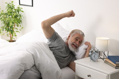 Emotional man raising fist and looking at alarm clock in bedroom