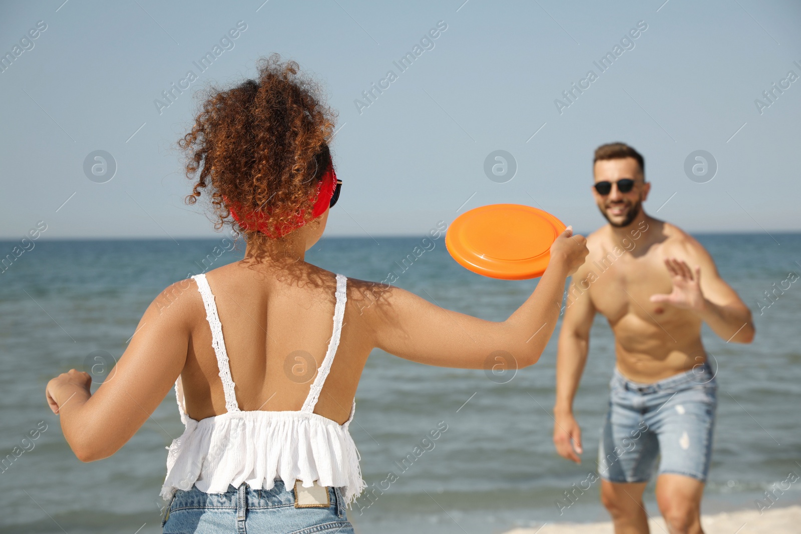 Photo of Couple playing with flying disk at beach on sunny day