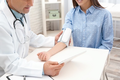 Doctor checking young woman's pulse with medical device in hospital, closeup