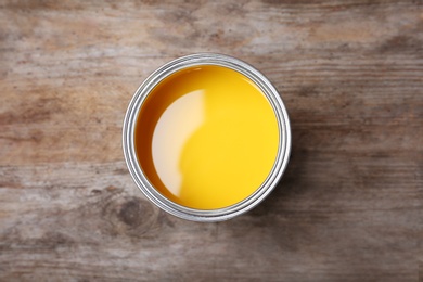 Photo of Can with yellow paint on wooden background, top view