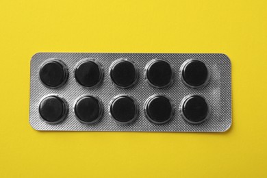 Photo of Activated charcoal pills in blister on yellow background, top view. Potent sorbent