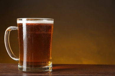 Mug with fresh beer on wooden table against dark background. Space for text