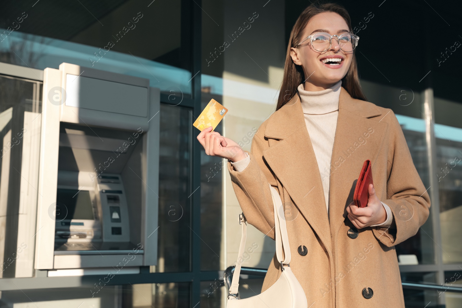 Photo of Excited young woman with credit card near cash machine outdoors