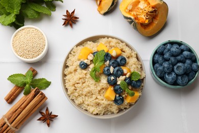 Photo of Flat lay composition with bowl of tasty quinoa porridge, blueberries and pumpkin on white tiled table