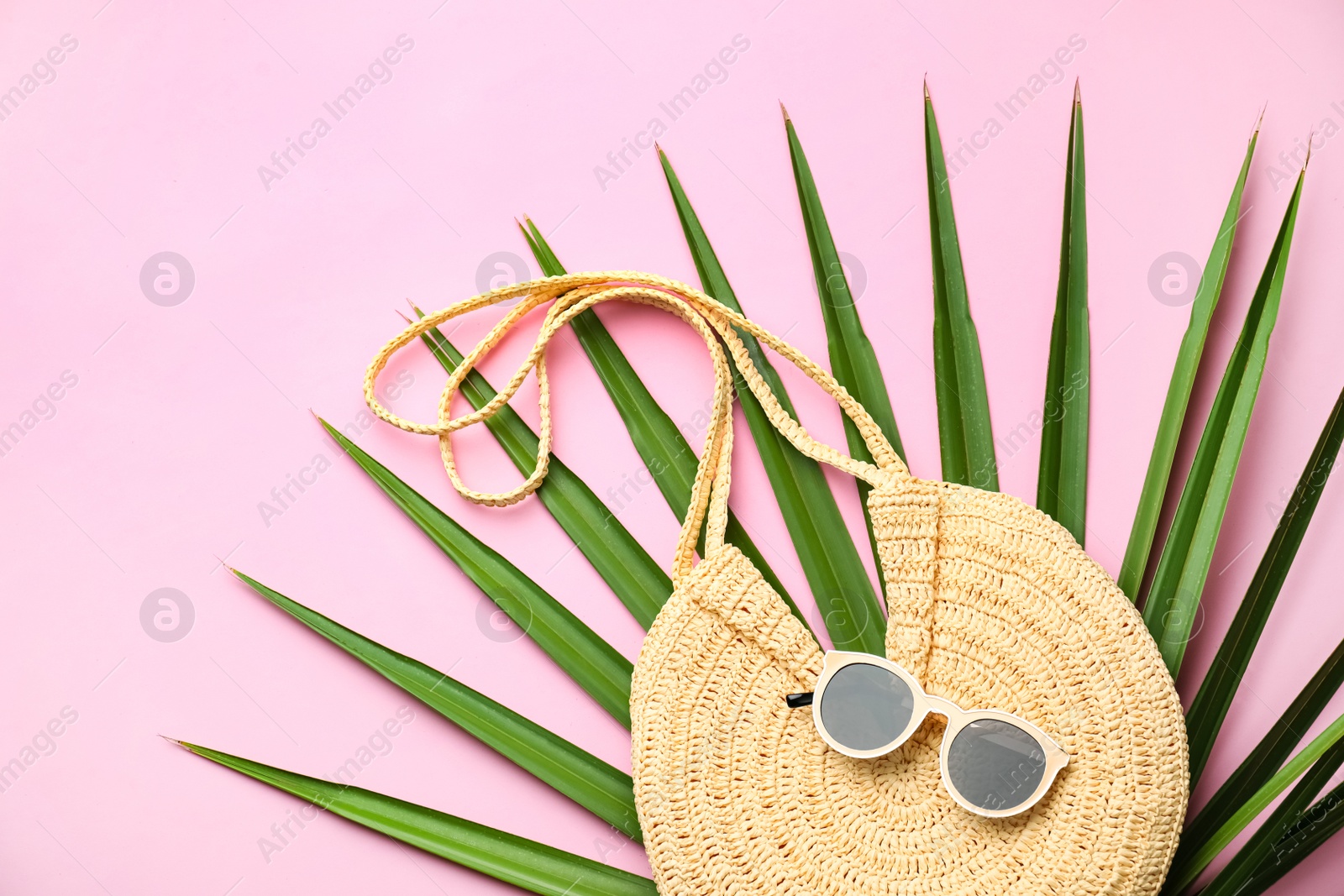 Photo of Elegant woman's straw bag with tropical leaf and sunglasses on pink background, top view