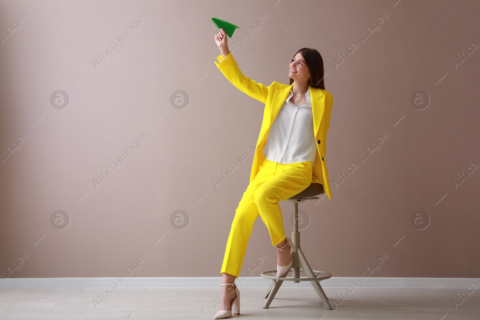 Photo of Beautiful teenage girl with paper plane near beige wall