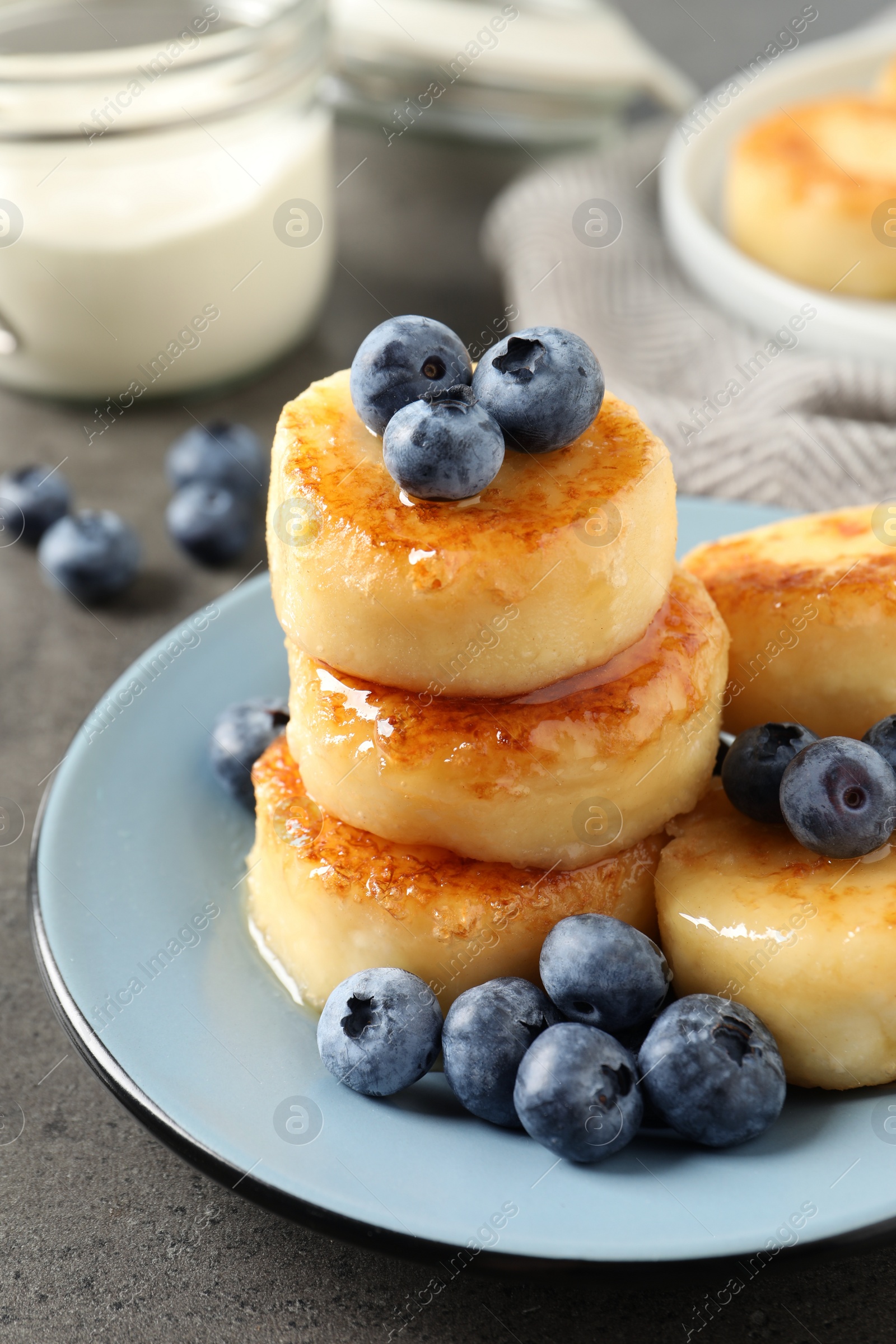 Photo of Delicious cottage cheese pancakes with blueberries and honey on grey table, closeup