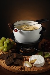 Photo of Forks with pieces of grape, bread, fondue pot with melted cheese and snacks on table