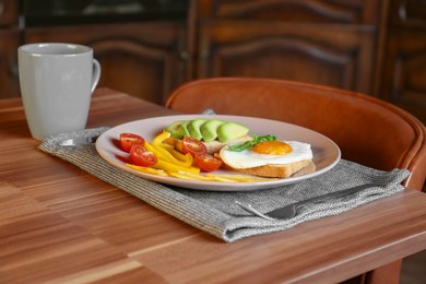 Photo of Tasty toasts with fried egg, avocado, cheese, vegetables and cup of coffee on wooden table indoors