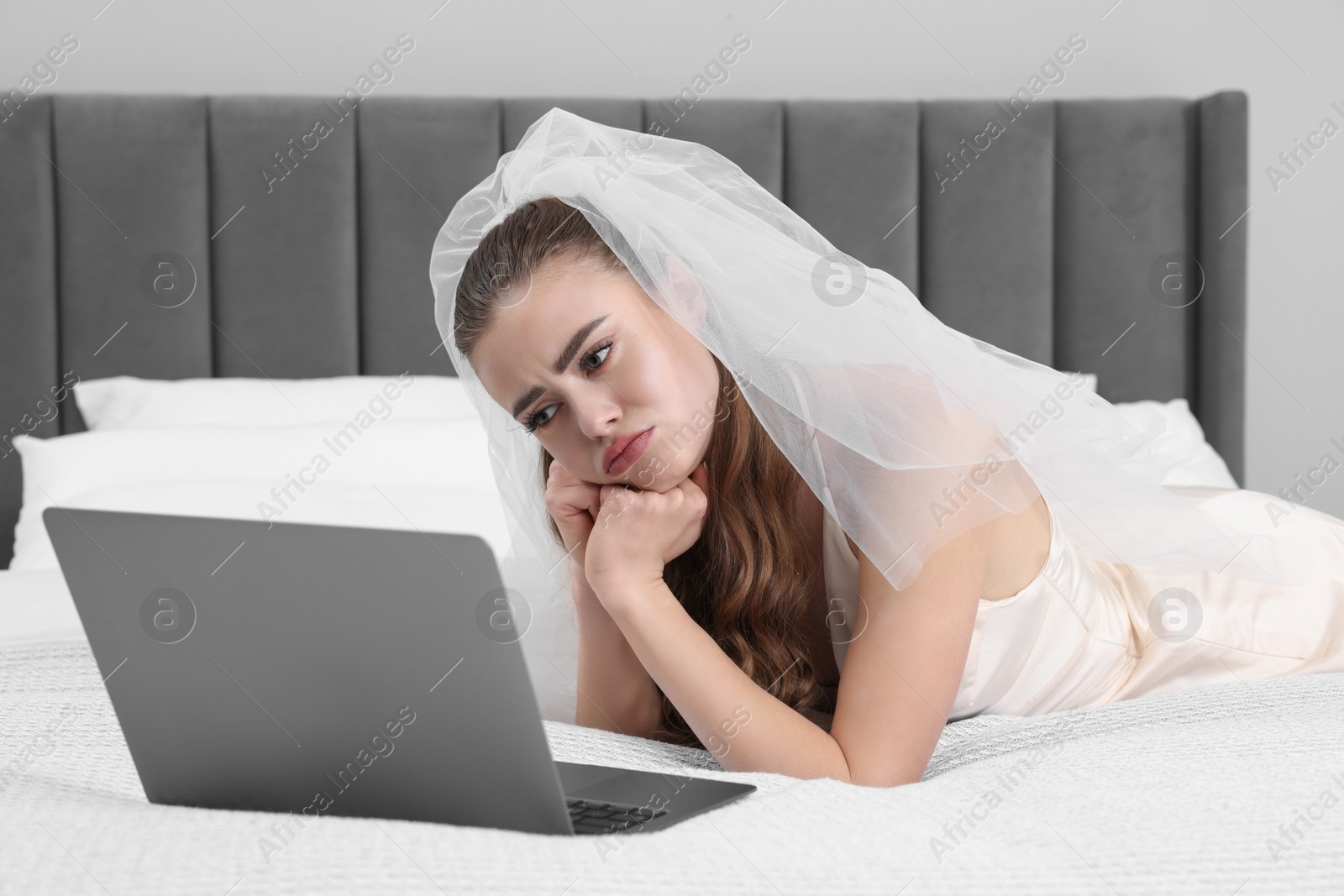 Photo of Upset bride with laptop on bed in bedroom