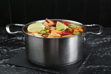 Photo of Saucepan with delicious Tom Yum soup on black marble table