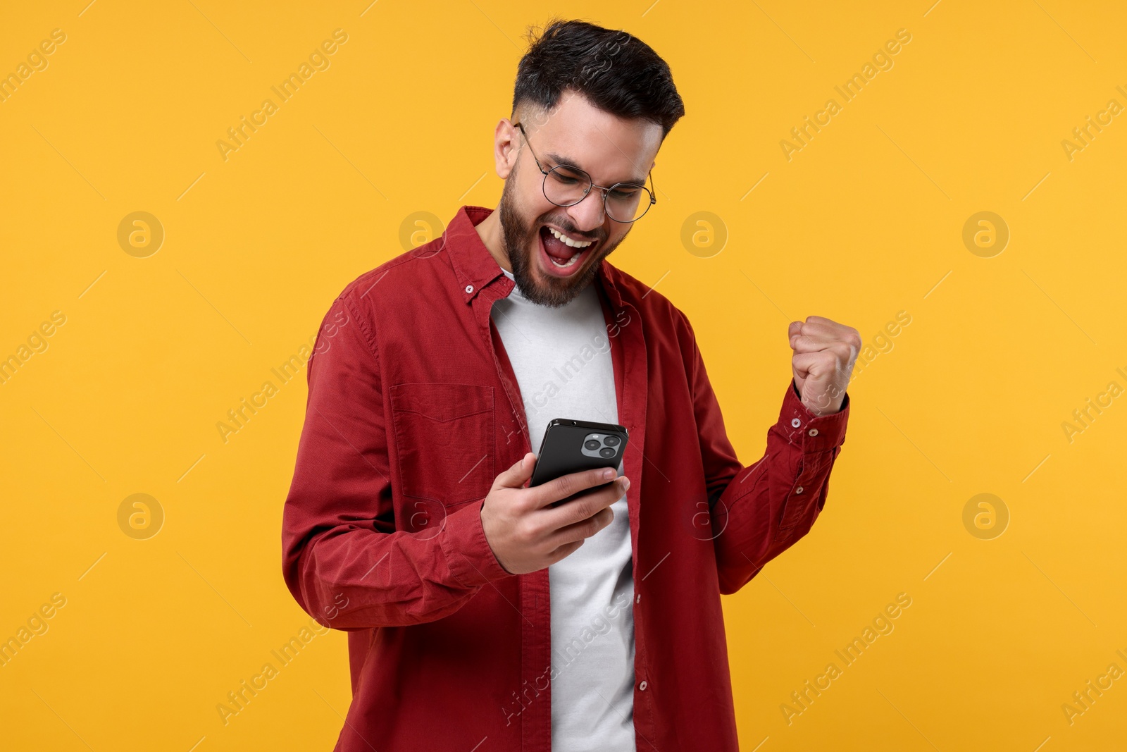 Photo of Happy young man using smartphone on yellow background