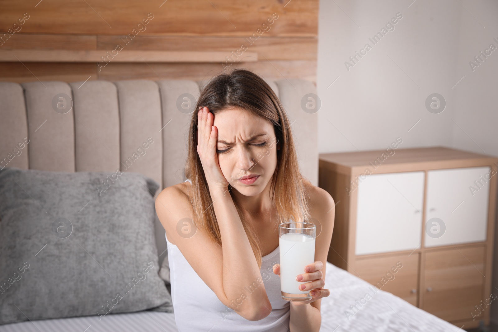 Photo of Woman holding glass of medicine for hangover on bed at home