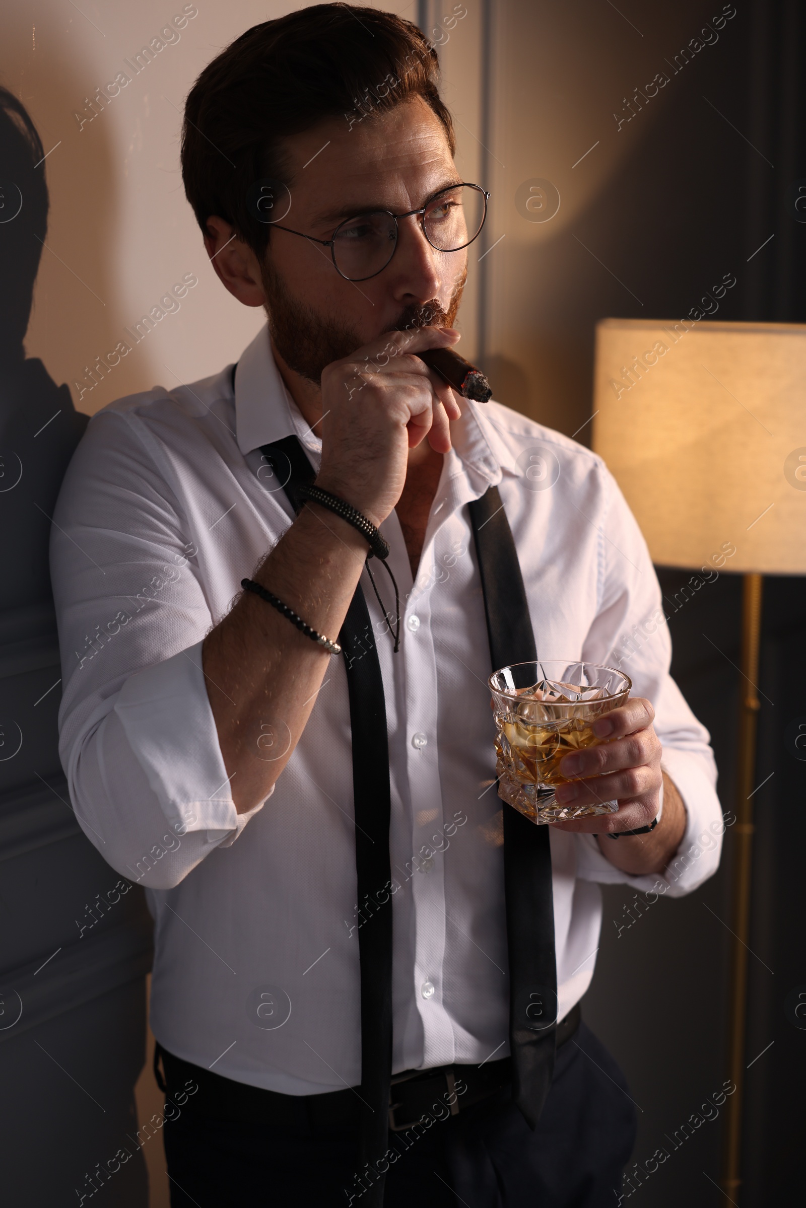 Photo of Handsome man with glass of whiskey smoking cigar at home