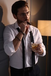 Handsome man with glass of whiskey smoking cigar at home