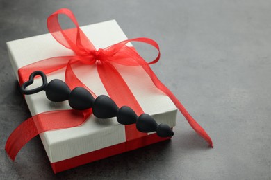 Photo of Black anal beads and gift box on grey table, space for text. Sex toy