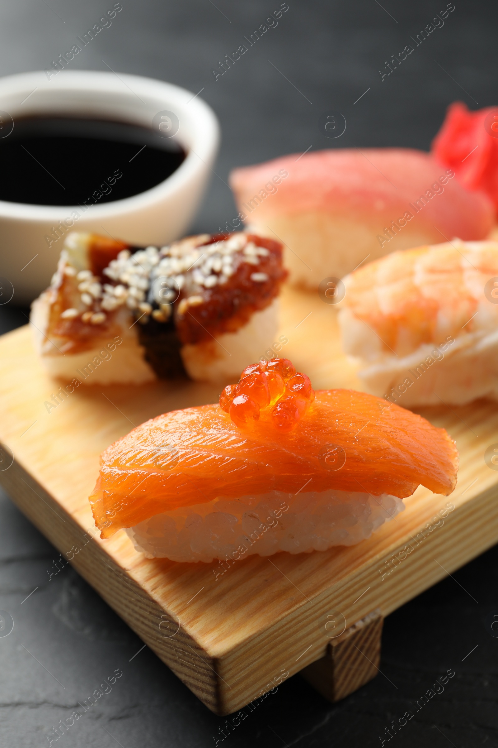 Photo of Wooden board with delicious nigiri sushi and soy sauce on black table, closeup