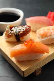 Photo of Wooden board with delicious nigiri sushi and soy sauce on black table, closeup
