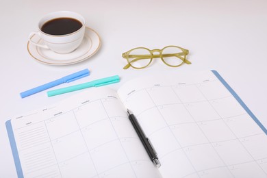 Photo of Open monthly planner, coffee, glasses and stationery on white background