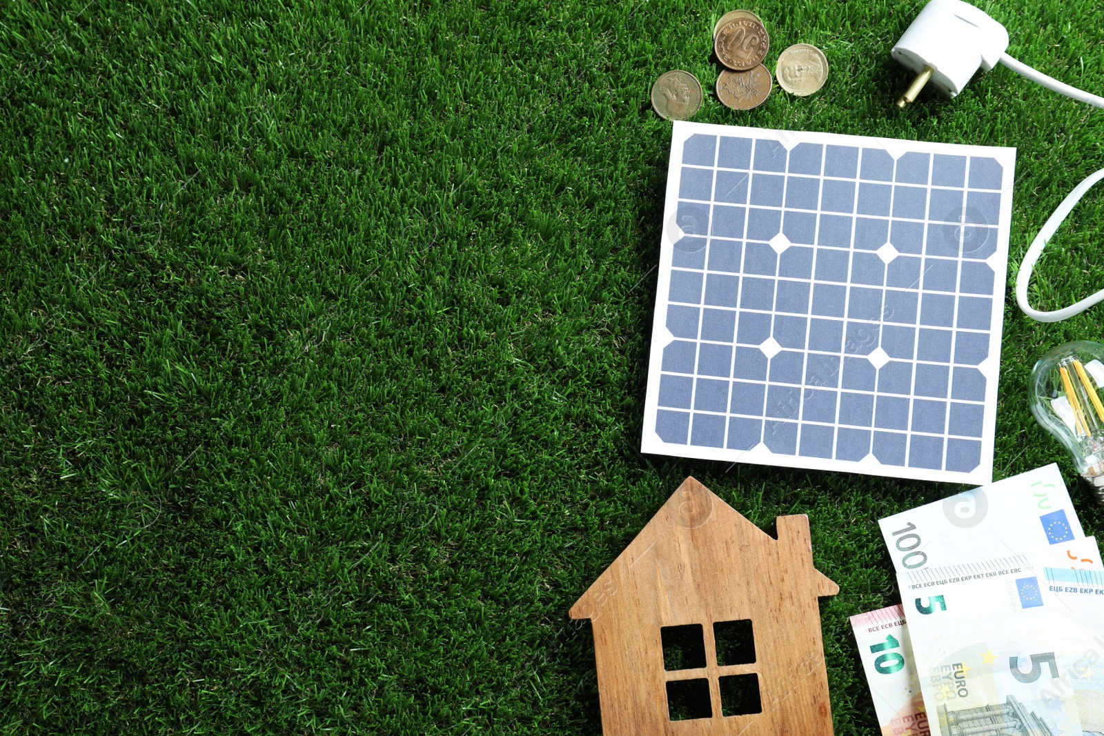 Photo of Flat lay composition with solar panel, house model and money on green grass. Space for text