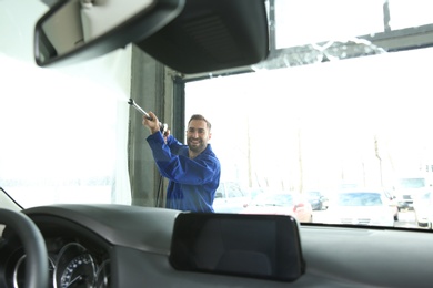 Photo of Worker cleaning automobile windshield with high pressure water jet at car wash, view from inside