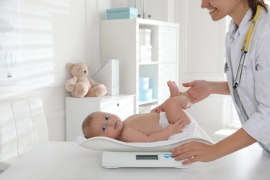 Photo of Pediatrician weighting cute baby in clinic, closeup. Health care