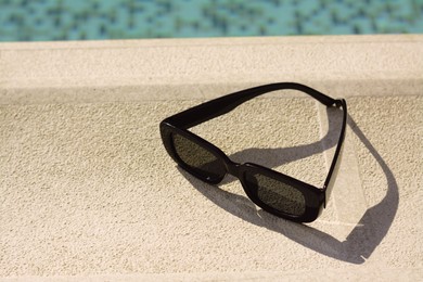 Stylish sunglasses near outdoor swimming pool on sunny day, space for text