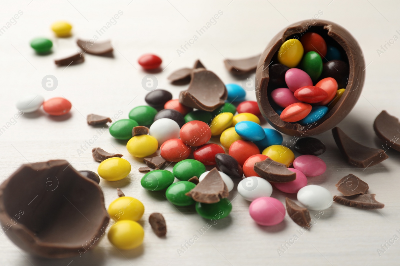 Photo of Broken chocolate egg and colorful candies on white table