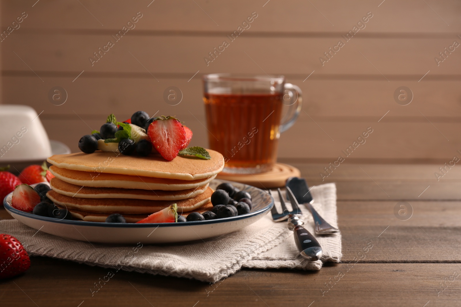 Photo of Delicious pancakes with fresh berries and butter served on wooden table, space for text