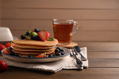 Delicious pancakes with fresh berries and butter served on wooden table, space for text