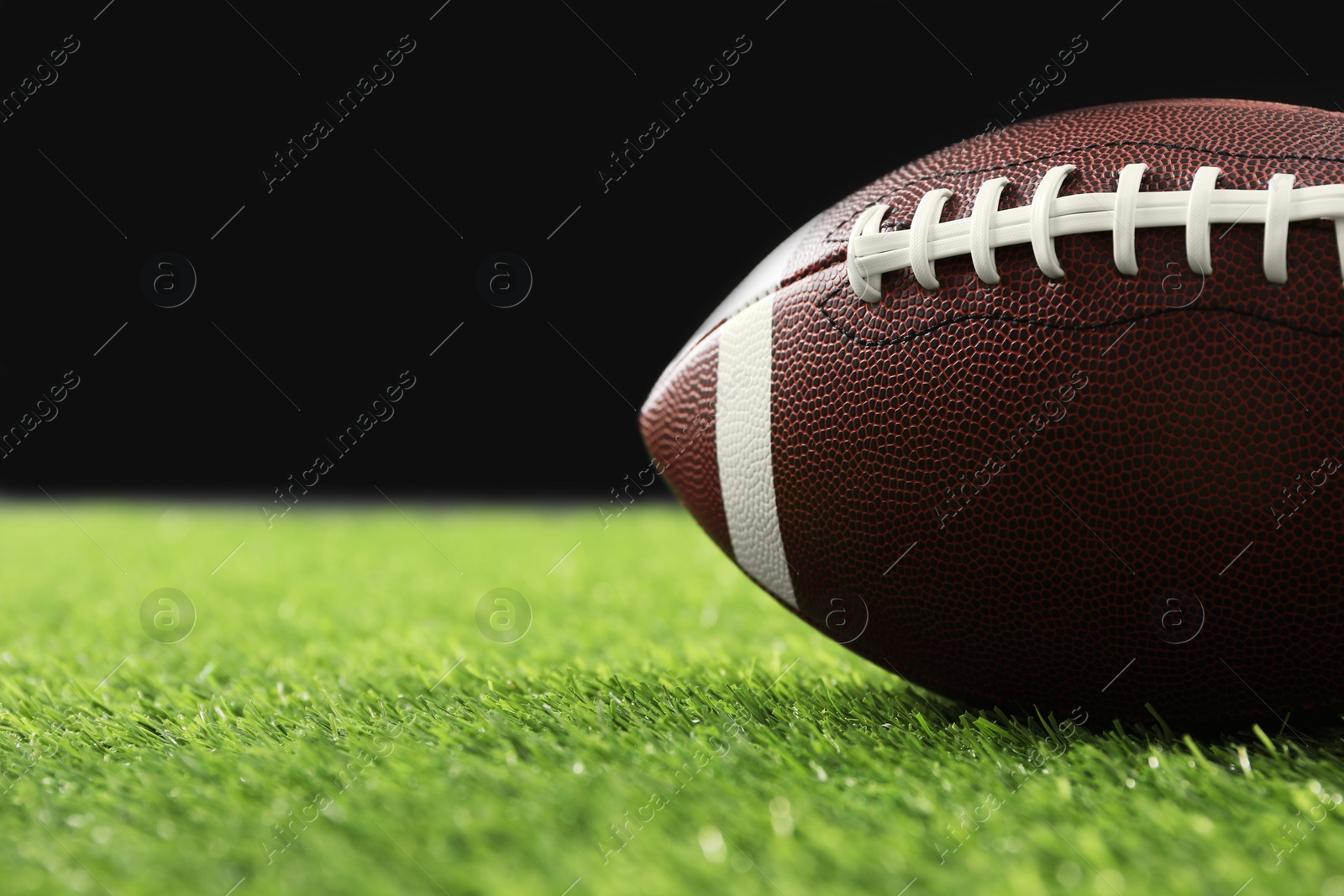 Photo of Rugby ball on green grass against black background, closeup. Space for text