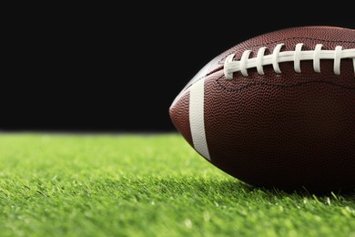 Rugby ball on green grass against black background, closeup. Space for text