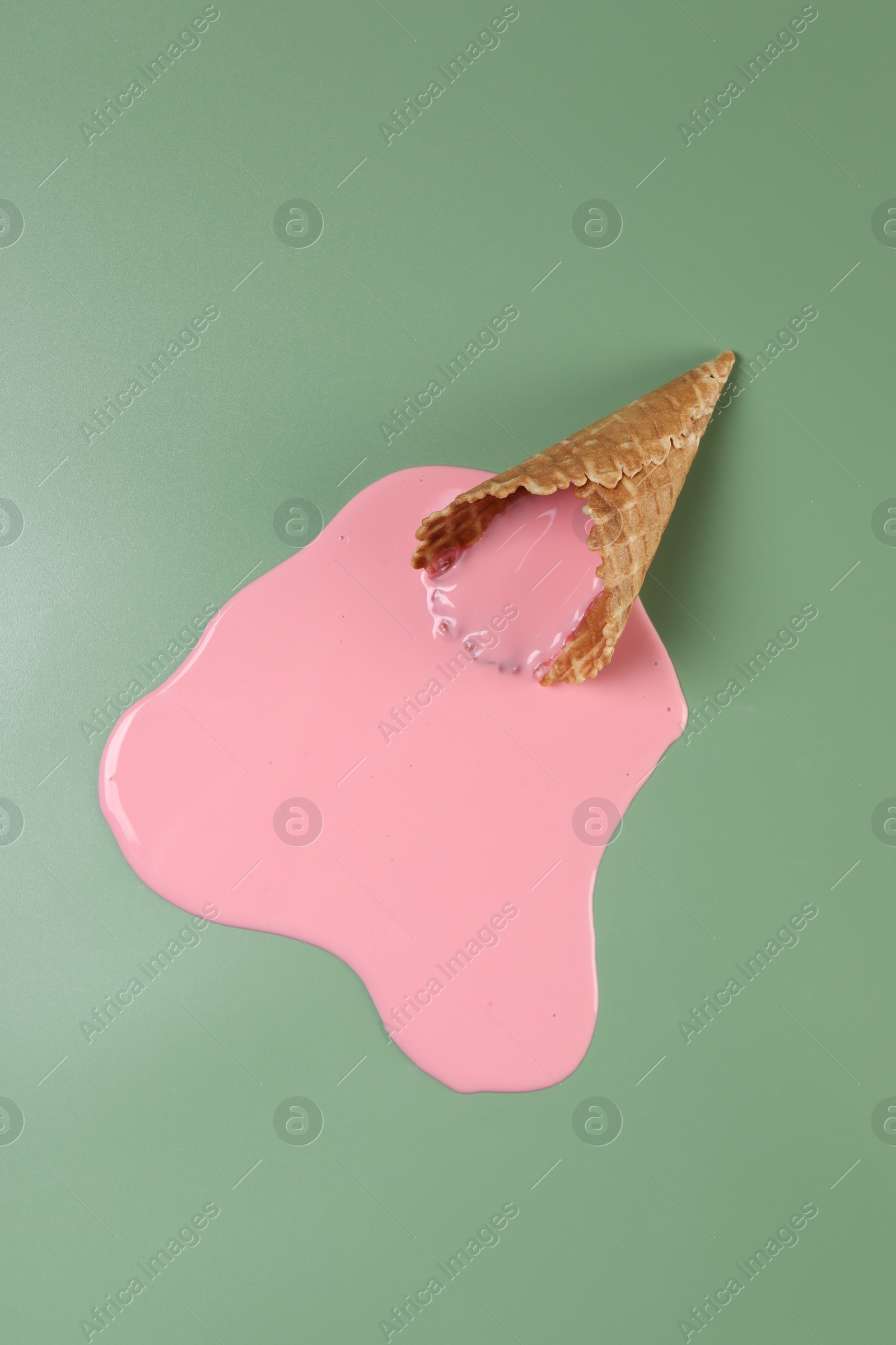 Photo of Melted ice cream and wafer cone on green background, top view