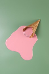 Melted ice cream and wafer cone on green background, top view