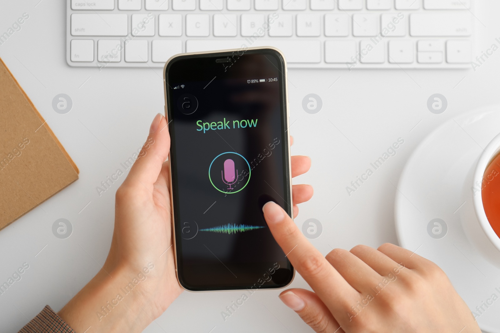 Photo of Woman using voice search on smartphone at white table, top view