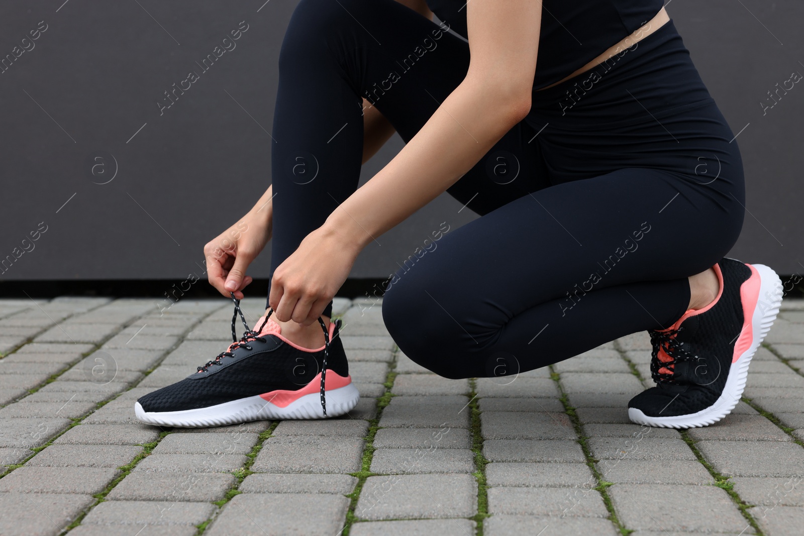 Photo of Woman tying shoelace of sneakers on street, closeup