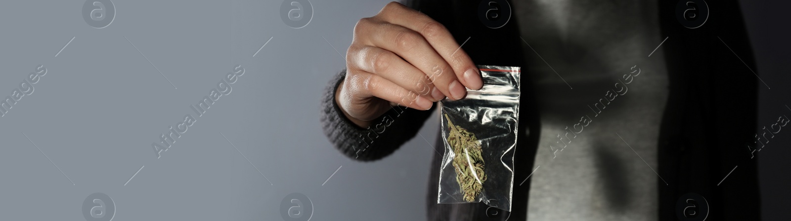 Image of Dealer holding hemp in plastic bag on grey background, closeup. Banner design with space for text