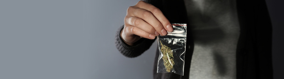 Image of Dealer holding hemp in plastic bag on grey background, closeup. Banner design with space for text