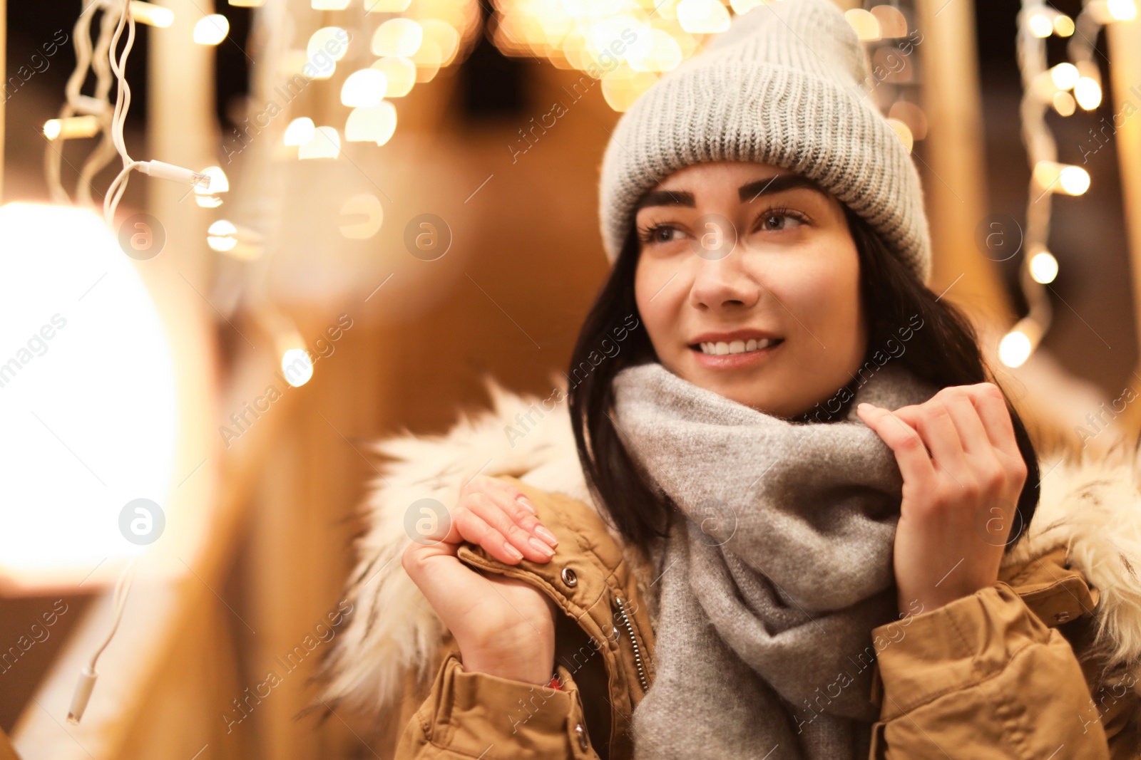 Photo of Beautiful young woman near festive lights outdoors. Winter vacation