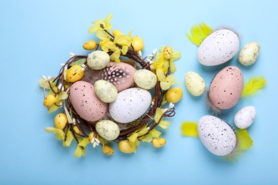Photo of Decorative nest with many painted Easter eggs on light blue background, flat lay