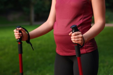 Photo of Pregnant woman practicing Nordic walking with poles outdoors, closeup