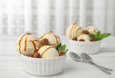 Photo of Delicious ice cream with caramel sauce and hazelnuts served on table. Space for text